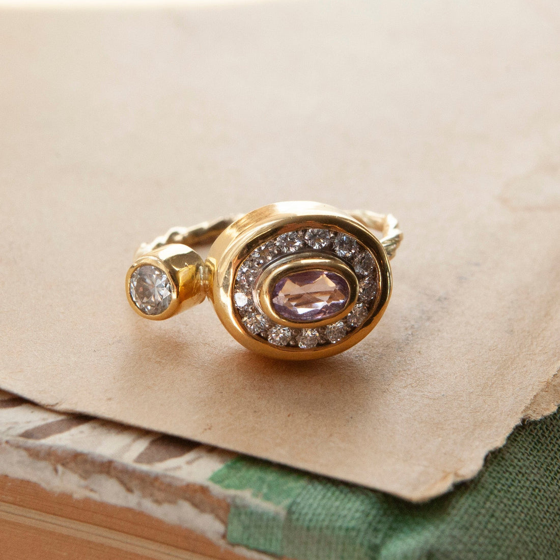 Gold ring with a pink gemstone and smaller diamonds on a textured surface